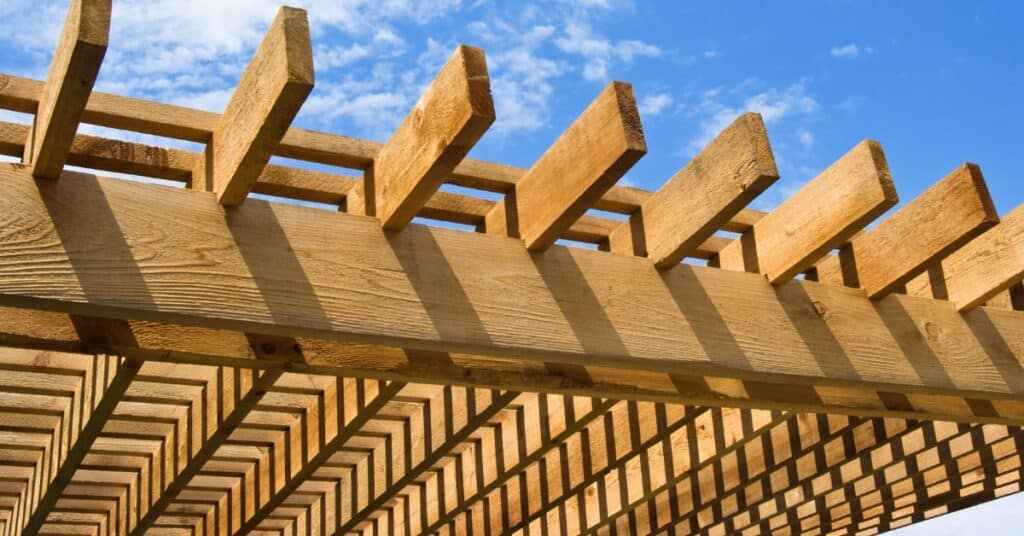 Close-up of a modern outdoor kitchen pergola made of natural wood beams under a blue sky